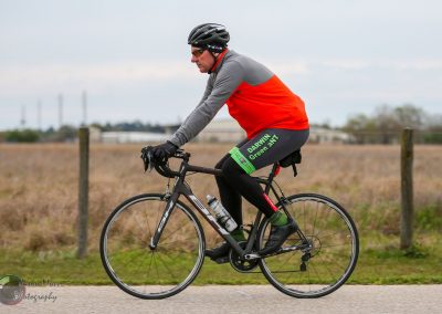 Bright cyclist on a road bike riding through open fields in Texas, promoting eco-friendly transportation with Bluebonnet Express.