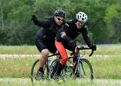 Riders enjoying a scenic bike ride through a grassy field with wildflowers and green trees in the background.