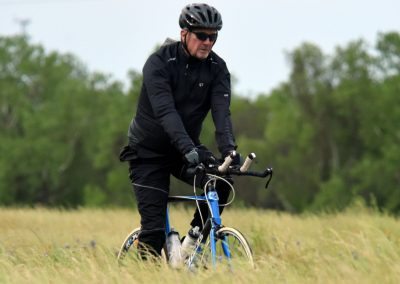 Comfortable cycling gear on a man riding a blue bike through grassy fields.