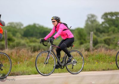 Bright pink cycling jacket on woman riding a bike outdoors during daytime, promoting Bluebonnet Express cycling event.