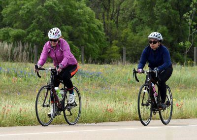 Vibrant women cycling in scenic meadow with wildflowers, enjoying outdoor bike ride.