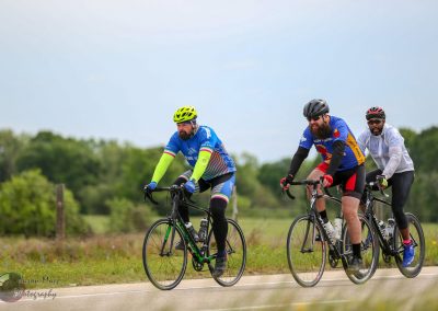Vibrant cyclists riding on open road during daytime, showcasing Bluebonnet Express eco-friendly biking event.