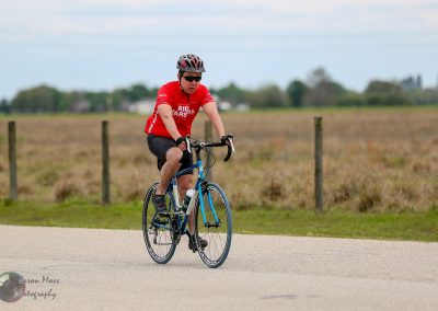 High-performance cyclist riding on gravel road in rural area, promoting Bluebonnet Express bike tours.
