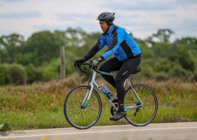 Bright blue and black cycling jacket, mountain bike, rider in motion on scenic outdoor trail, promoting Bluebonnet Express bike routes.
