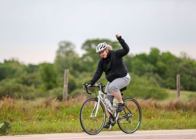 Bright woman cycling on scenic rural bike path, promoting Bluebonnet Express bicycle services.