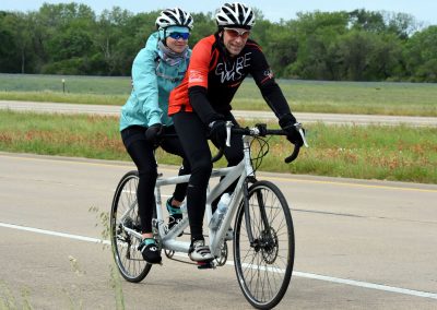 Riders enjoying a scenic bike ride on a tandem bicycle in a lush green landscape.