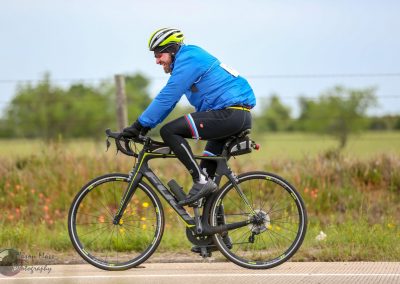 Bright blue cycling jacket and black bike with neon yellow accents on an outdoor path.
