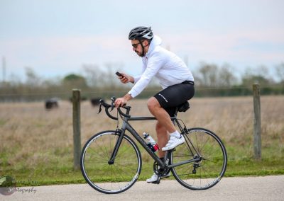 Rider using phone on a sleek black road bike on a scenic outdoor trail.