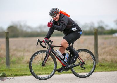 Fast cyclist riding a black and red road bike outdoors on a cloudy day, promoting Bluebonnet Express cycling services.