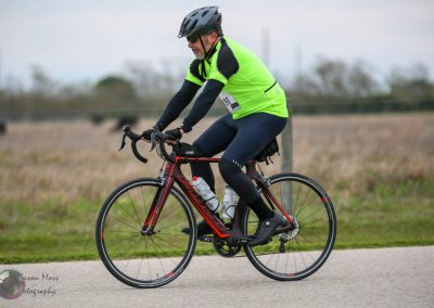 1. Man riding a black and red road bike in outdoor cycling event, wearing neon green safety vest and helmet.