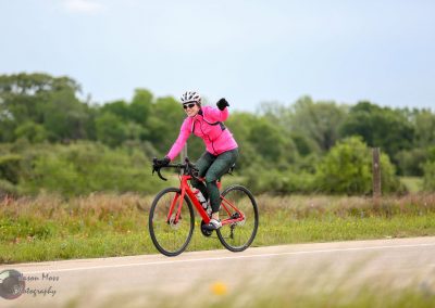 Bright pink cycling jacket on woman riding a red bike on scenic countryside trail.