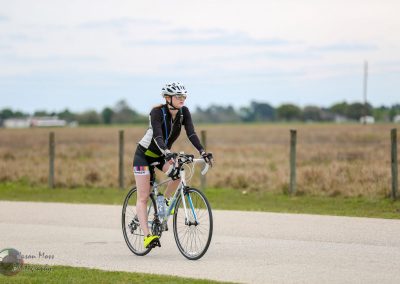 Youth female cyclist riding bike outdoors on rural road, wearing helmet and sports attire.