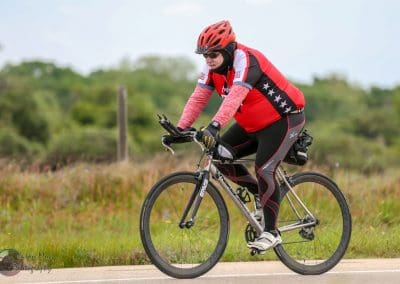 Overweight cyclist riding a bike on a scenic outdoor trail in a red and black uniform.