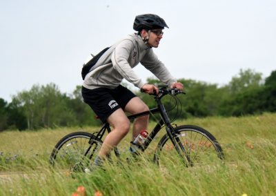 Vibrant outdoor scene of a man cycling through a grassy field with wildflowers, emphasizing adventure and outdoor biking.