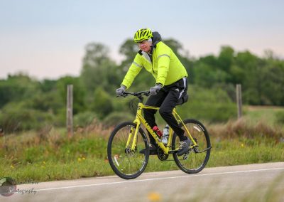 Bright yellow bicycle on scenic rural road with cyclist wearing high-visibility gear, promoting Bluebonnet Express bike service.