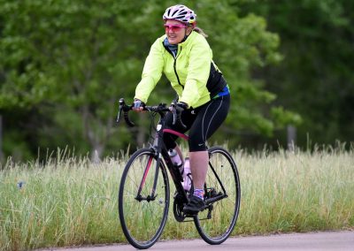 Bright yellow cycling jacket and helmet worn by woman riding a bicycle in a natural park setting.