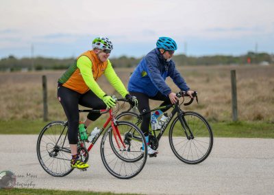 Smiling cyclists riding on a scenic country road in colorful cycling gear for Bluebonnet Express event.