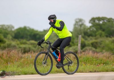 Vivid cyclist in neon jacket on rural bike trail, experiencing a flat tire emergency.