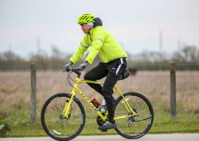 Bright yellow bike and rider in high-visibility jacket riding outdoors on a scenic trail.