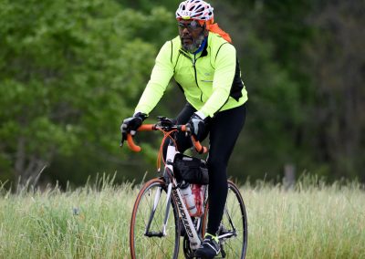 Vibrant cyclist in neon yellow jacket riding through grassy field for Bluebonnet Express event.