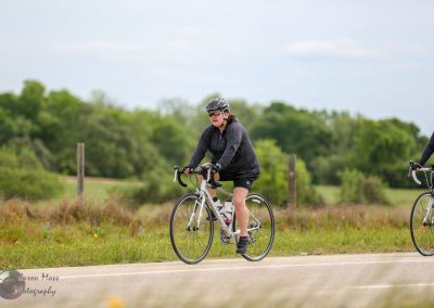 Bright woman cycling on a scenic rural road in Texas, promoting Bluebonnet Express bike tour.