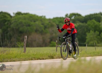 Vibrant cyclist riding on rural road with lush green trees in background.