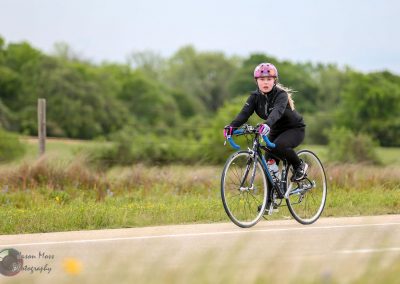 Bright young woman cycling on scenic rural road with lush greenery, promoting Bluebonnet Express bike service.