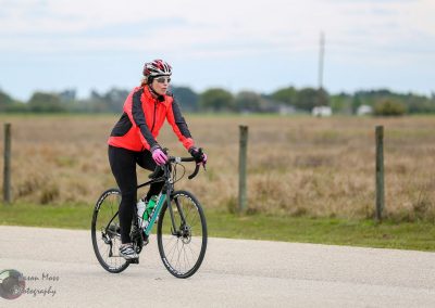 Vibrant woman cycling on a scenic open road, promoting Bluebonnet Express bike tours for outdoor adventures.