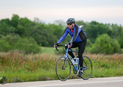 Bright blue road bike rider on scenic outdoor trail with Green trees, promoting Bluebonnet Express cycling service.