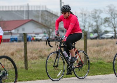 Bright pink cycling jersey on woman riding a black road bike outdoors.