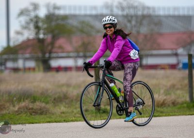 Bright pink cycling jacket woman riding bike during outdoor event, smiling, wearing helmet, sunglasses, and leggings, promoting Bluebonnet Express.