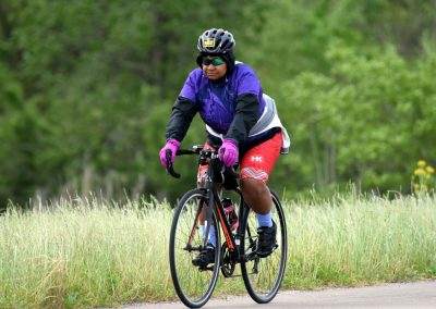 Vibrant cyclist riding on scenic trail surrounded by green trees and grass, enjoying a bike ride.