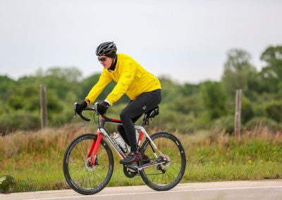 Vibrant cyclist in yellow jacket riding a red and black bike on scenic road, outdoor biking adventure with Bluebonnet Express.