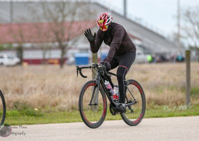 High-performance cyclist wearing a helmet and sunglasses on a black road bike during a race.