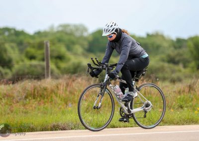 Bright woman cycling on rural road with scenic greenery, promoting Bluebonnet Express bike tours and eco-friendly transportation.