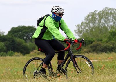 Vibrant cyclist in green jacket riding Bluebonnet Express bike through grassy field during daytime.