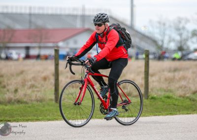 Rider on a road bike participating in outdoor cycling event, wearing red jacket, helmet, sunglasses.