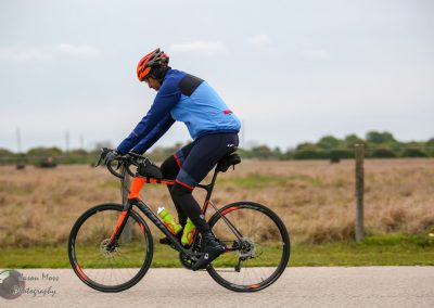 Bright orange and black bicycle with a rider in cycling gear on an outdoor road.