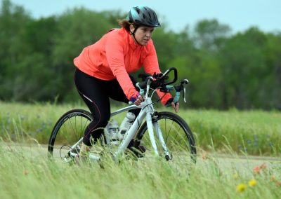 Bright woman riding a gravel bike on nature trail in outdoor park.