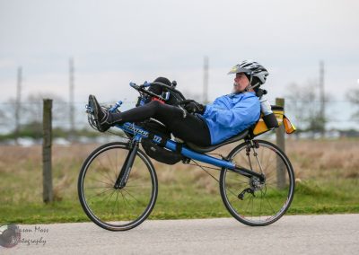 Man lying on a recumbent bicycle with bicycle touring gear outdoors.