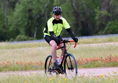 Bright yellow and black cycling jacket on male cyclist riding in scenic outdoor field with colorful flowers.