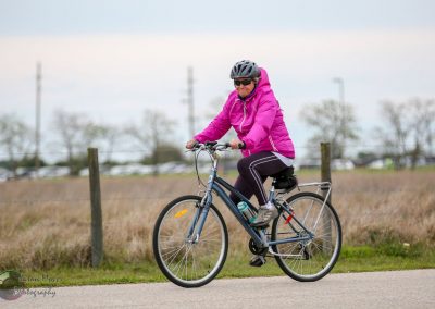 Bright pink jacket woman riding bicycle during daytime in open field for Bluebonnet Express event.
