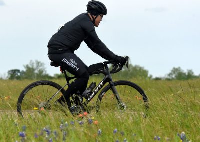 Bright cyclist riding a bike through a meadow with wildflowers, exploring Bluebonnet Express scenic routes.