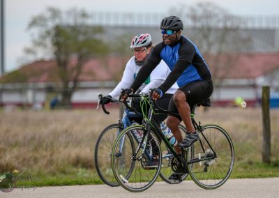 Bright blue and black cycling jerseys on two cyclists riding together outdoors on a cloudy day.