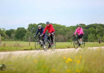 Comfortable women’s cycling trip on a rural Texas road with lush greenery and blooming wildflowers.