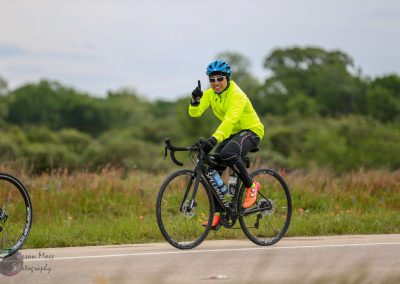 Vibrant cyclist in neon yellow jacket biking on scenic road, promoting Bluebonnet Express bike service.