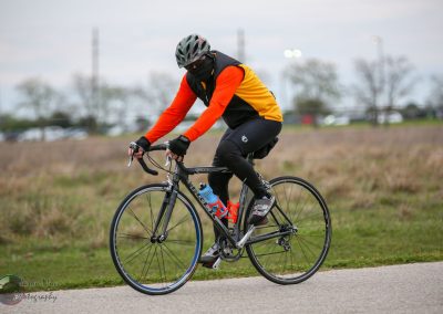 Bright cyclist riding a road bike on a paved trail during daytime.