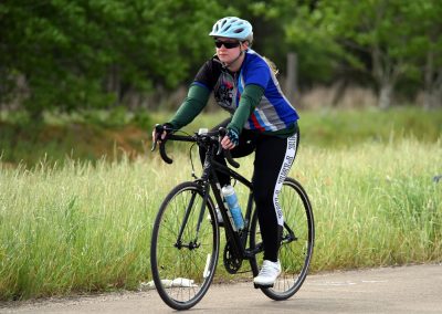 Girl biking on trail with Bluebonnet Express logo, sunny outdoor cycling adventure.