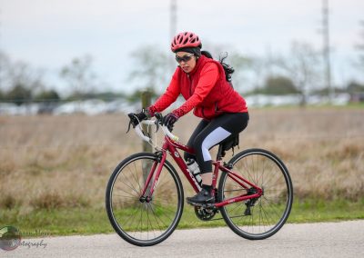 Bright red cycling helmet and jacket on woman riding a bike outdoors for Bluebonnet Express event.