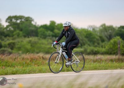 A woman cycling outdoors during daylight on a scenic trail with lush greenery.